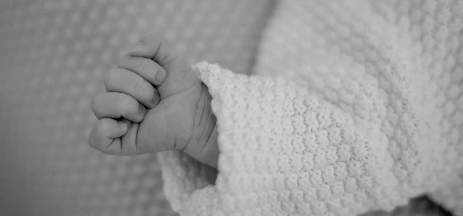 Schwarz-Weiß-Aufnahme: die kleine Hand eines Neugeborenen umfasst einen Finger